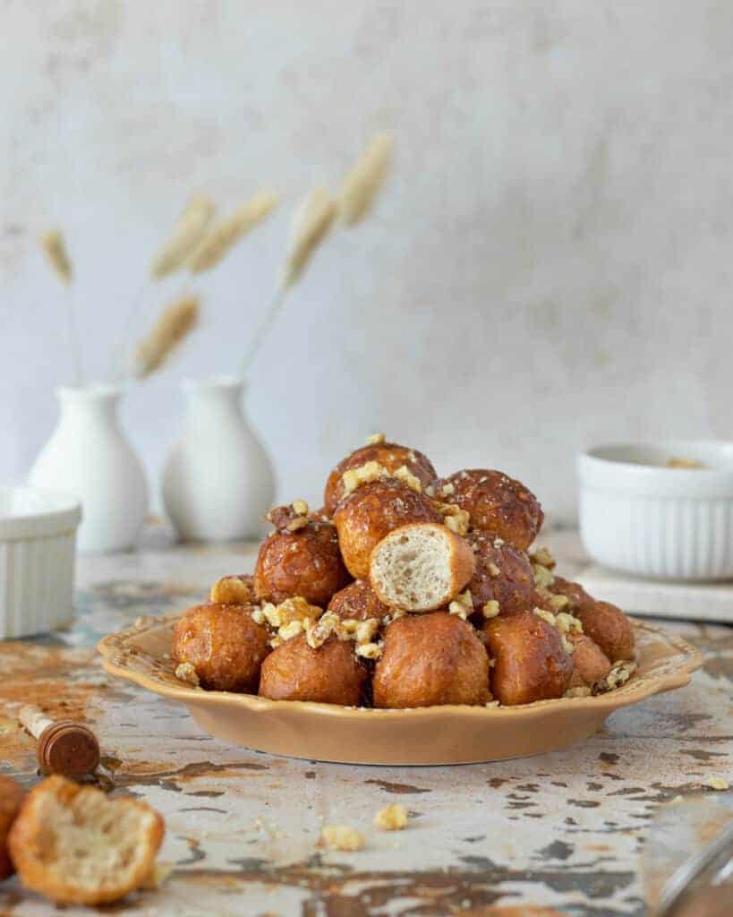 Loukoumades erved on a plate with honey, cinnamon and walnuts.