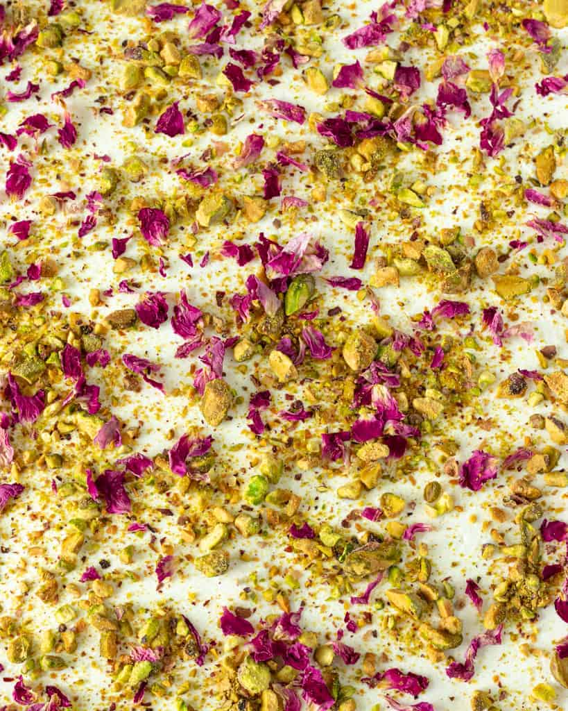 Closeup of pistachios and rose petals on top of whipped cream.