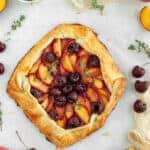 Overhead shot of peach cherry galette surrounded by cherries and sliced peaches.