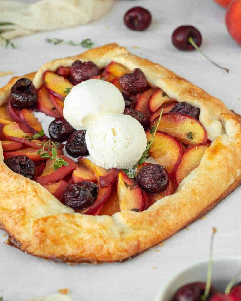 Close up shot of peach and cherry galette topped with two scoops of vanilla ice cream.