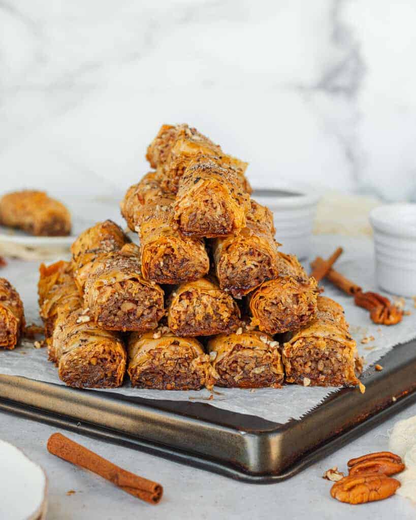 All pieces of baklava rolls shaping a pyramid on top of a baking pan lined with parchment paper.