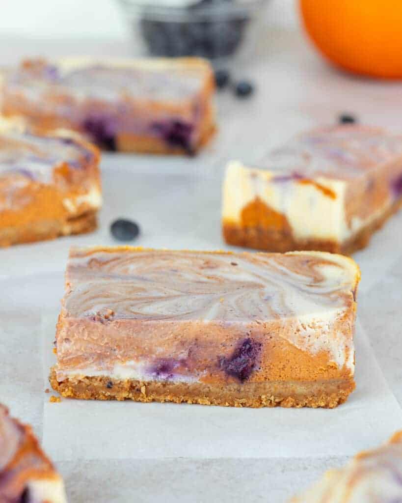 Straight up shot of pumpkin blueberry swirl cheesecake bar on parchment paper.