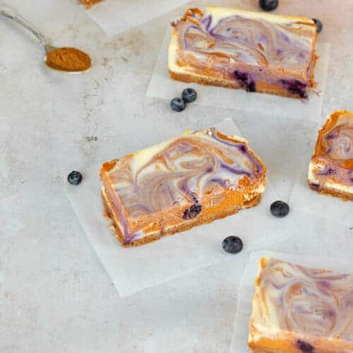 Pumpkin Blueberry Swirl Cheesecake Bars sliced and placed on parchment paper.