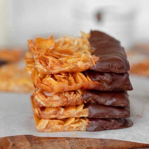 Chocolate florentine cookies stack on a wooden cutting board.