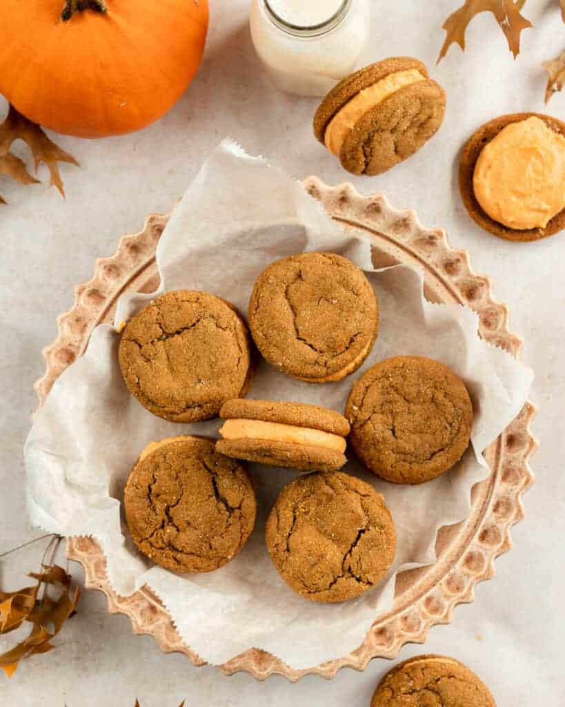 Overhead shot of soft molasses sandwich cookies surrounded from a pumpkin, Fall leaves and a milk jar.