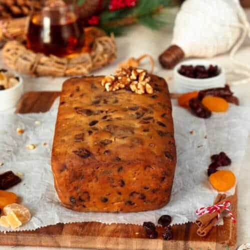 Rum soaked fruit cake on a dark background topped with walnuts.