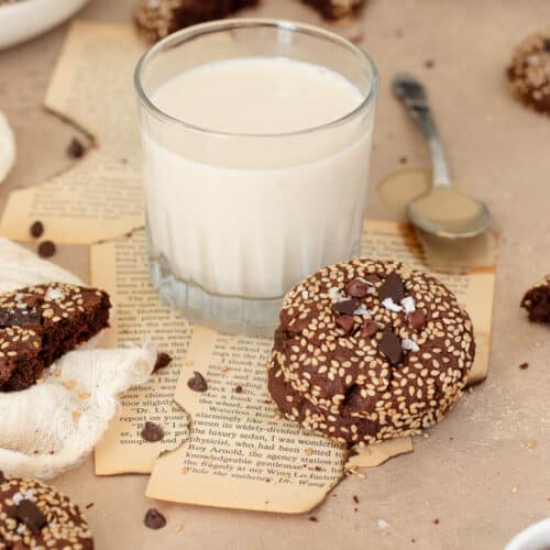 Photo of double chocolate tahini sesame cookies stacked next to a glass of milk.