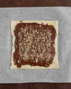 Photo of puff pastry dough spread with hazelnut spread and chopped hazelnuts.