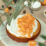 Photo of the clementine olive oil cake topped with yogurt frosting and fresh clementines.